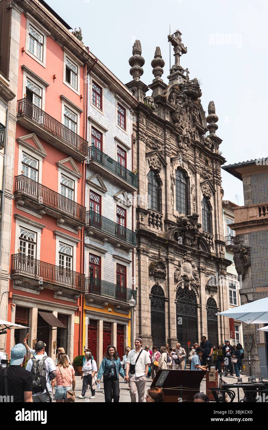 I turisti passano davanti all'ornata Igreja dos Clerigos barocca e ai vibranti edifici storici in una vivace scena di Porto Street. Porto, Portogallo - 11 giugno 2025 Foto Stock