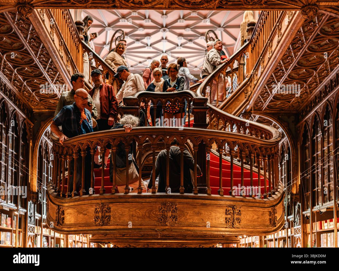 Folle di visitatori ammirano l'intricata scalinata in legno e l'architettura storica all'interno di Livraria Lello, una famosa libreria di Porto, Portogallo - 11 giugno 2025 Foto Stock