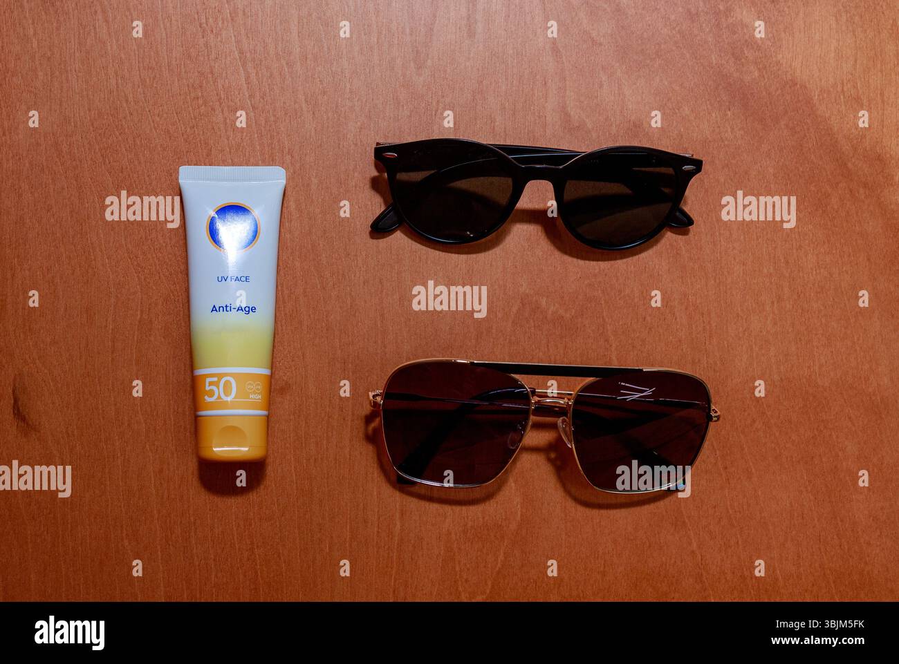 Piatto di crema solare e due paia di occhiali da sole disposti su sfondo in legno. Foto Stock