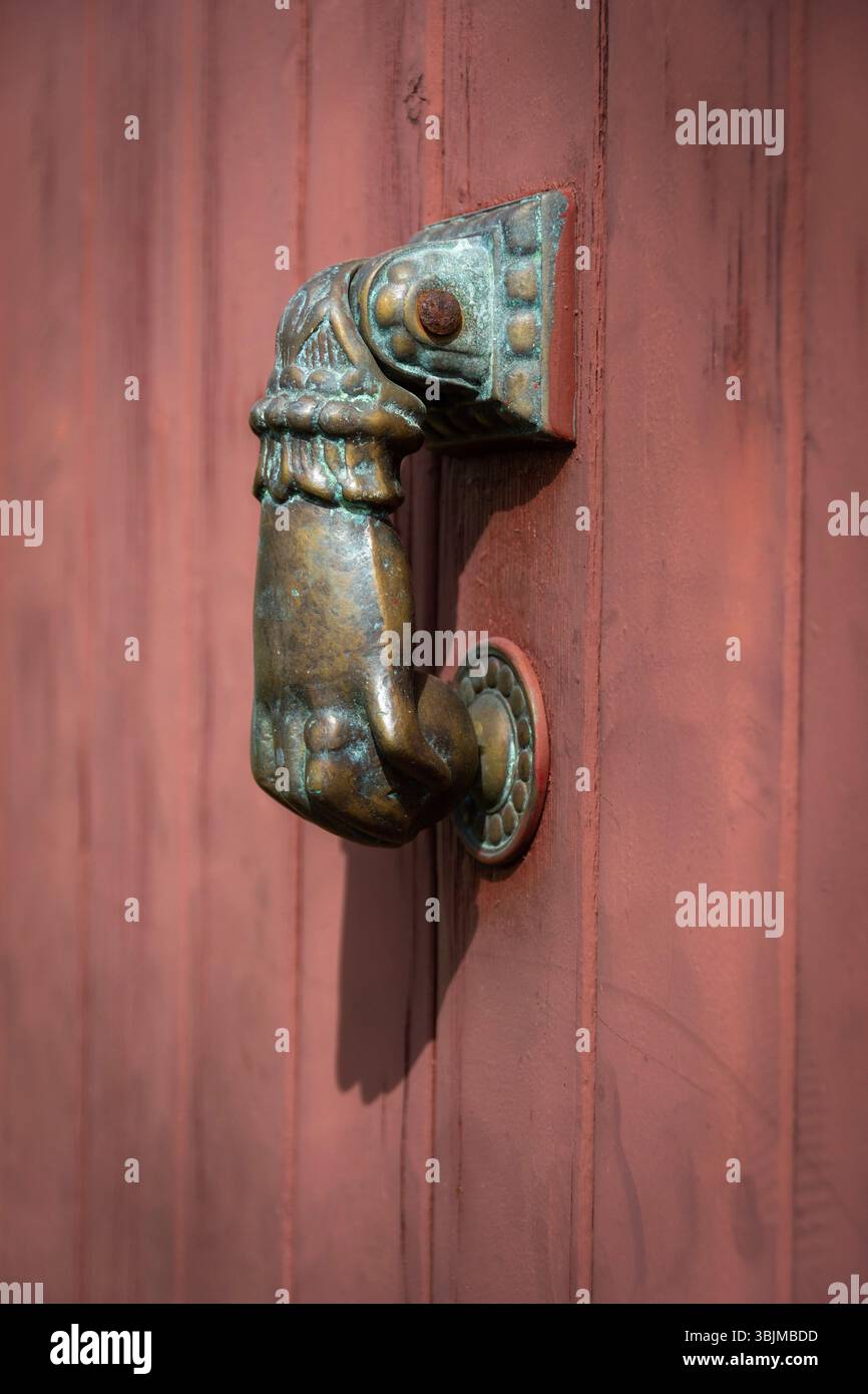 Un distintivo battente a forma di mano è applicato su una porta di legno rossa. Il design intricato e la lucentezza in bronzo aggiungono carattere all'ingresso. Francia Foto Stock