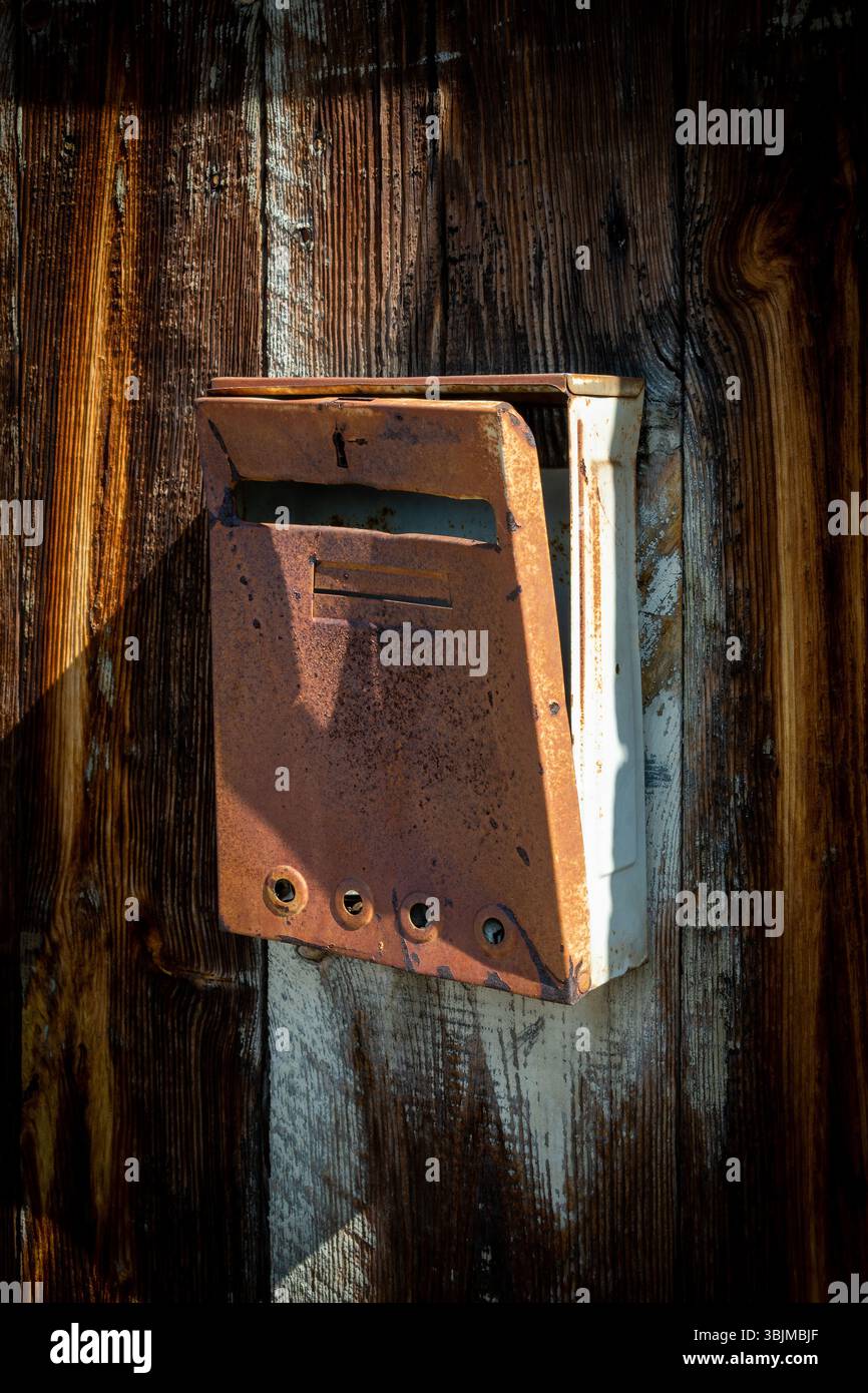 Una cassetta postale d'epoca è montata su una recinzione in legno resistente agli agenti atmosferici, inondata dalla calda luce del sole. Puy de Dome, Auvergne, Francia Foto Stock
