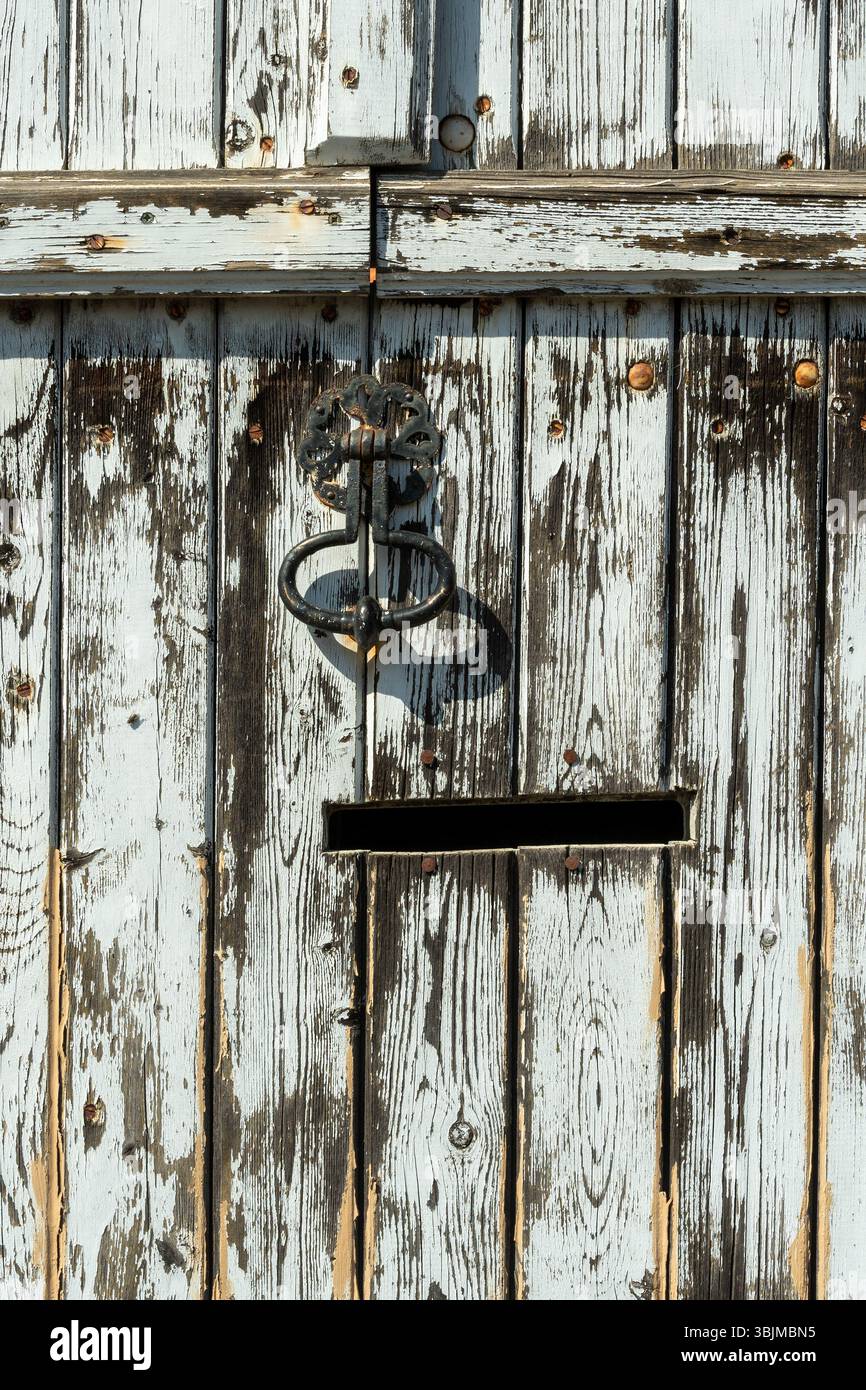 Una porta realizzata in tavole di legno intemperie presenta vernice blu sbucciante e una maniglia decorativa in metallo Foto Stock