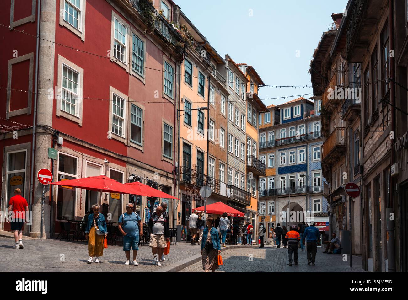 Vivace scena di strada cittadina con persone che camminano davanti a vecchi edifici colorati e caffetterie all'aperto, perfetto per ispirarsi ai viaggi. Porto, Portogallo - 11 giugno 2025 Foto Stock