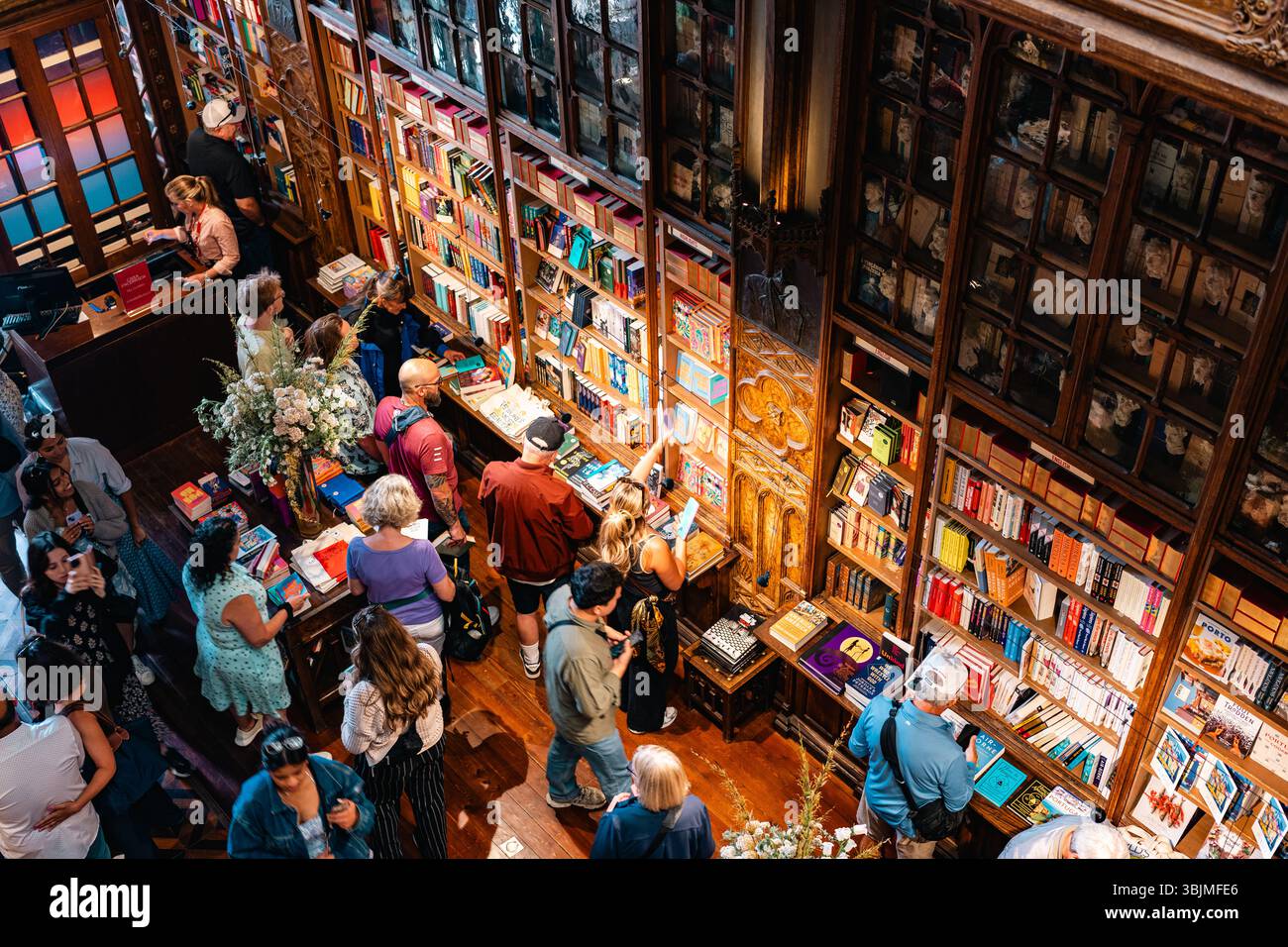 I turisti e la gente del posto sfogliano i libri all'interno di una famosa libreria ornata con scaffali in legno e un'atmosfera vivace. Porto, Portogallo - 11 giugno 2025 Foto Stock