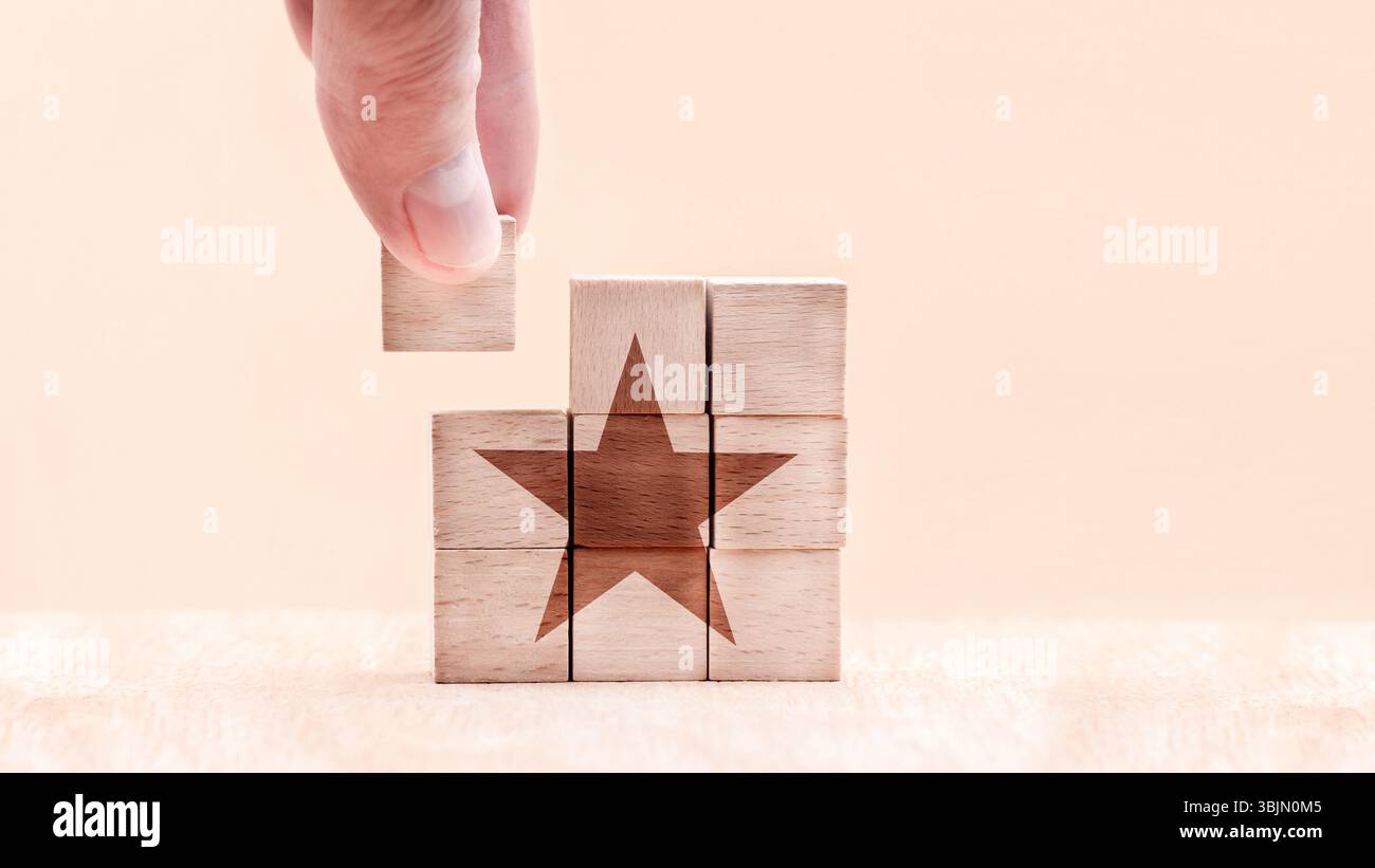 Una mano posiziona un blocco di legno per completare un puzzle di blocchi di legno con il simbolo di una stella. Questo simboleggia la creatività, il lavoro di squadra e l'innovazione. Il Foto Stock