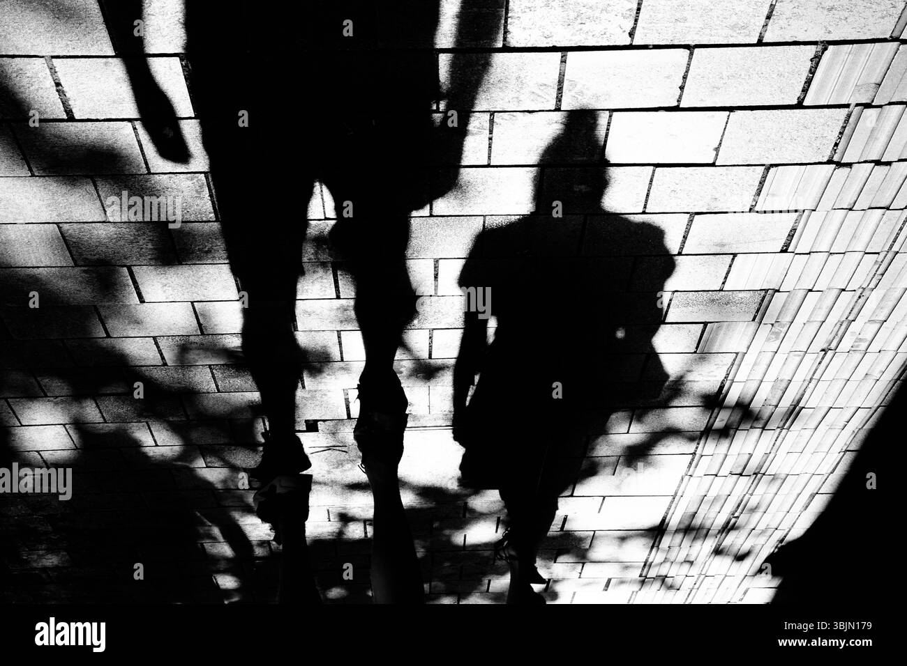 Silhouette ombrosa di uomo e donna che camminano lungo la strada della città marciapiede in bianco e nero a contrasto elevato Foto Stock