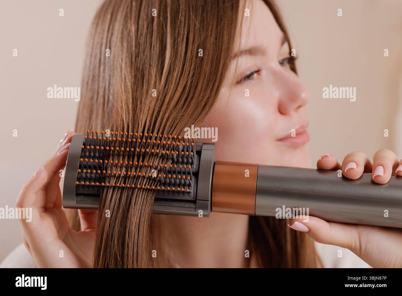 Primo piano di una donna che utilizza una moderna spazzola elettrica per lo styling dei capelli per lisciare e lisciare i suoi capelli lunghi e sani a casa, mostrando un beaut innovativo Foto Stock