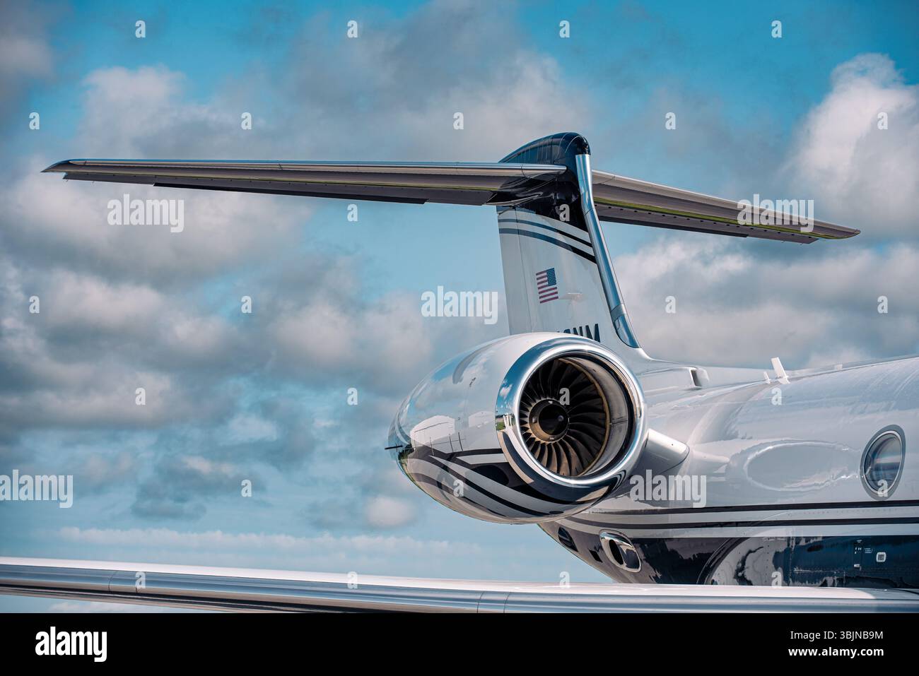 Motore jet e coda a T di un lussuoso business jet Gulfstream sotto cieli parzialmente nuvolosi. Fusoliera lucidata e dettagli della turbina chiaramente visibili. Foto Stock