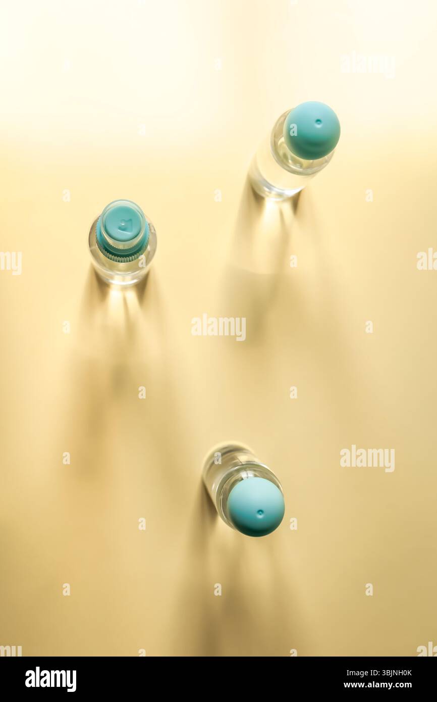 Vista dall'alto verso il basso di tre biberon da viaggio con tappi blu che proiettano ombre morbide su sfondo pastello. L'illuminazione ad alta luminosità crea un ambiente da sogno, pulito e moderno Foto Stock