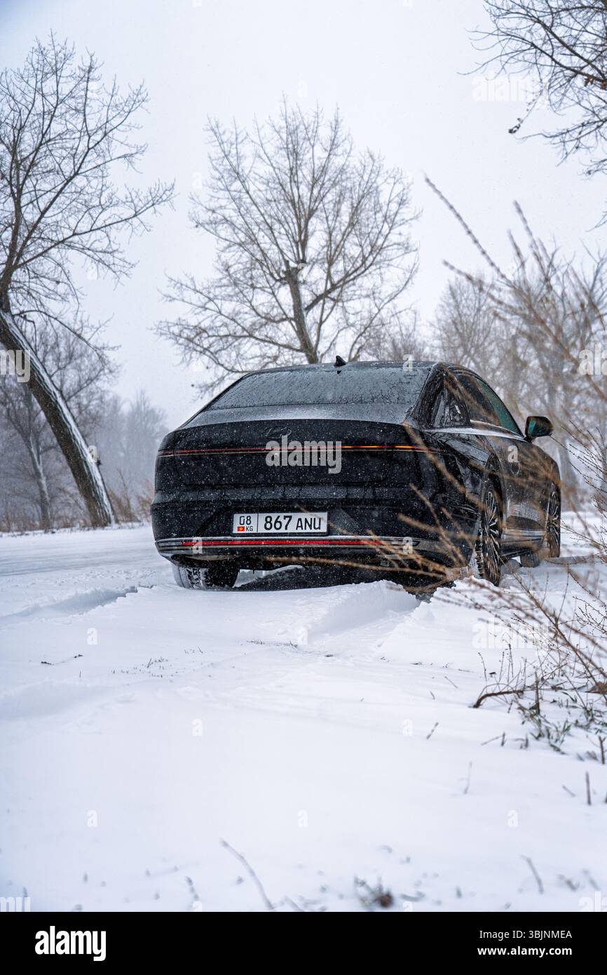 Bishkek, Kirghizistan - 12 dicembre 2024: Vista dall'angolo posteriore di una grandiosità Hyundai nera 2023 (GN7) su una strada innevata con alberi Foto Stock