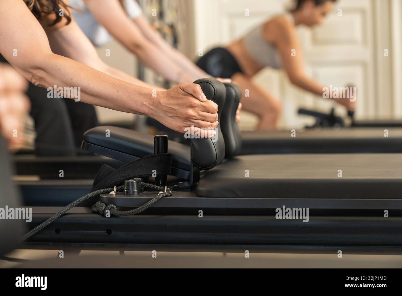 Una fila di atleti in un allenamento sincronizzato su macchine riformatrici durante una lezione di pilates di gruppo. Concentratevi sull'impegno coordinato e sulla comunicazione del fitness Foto Stock