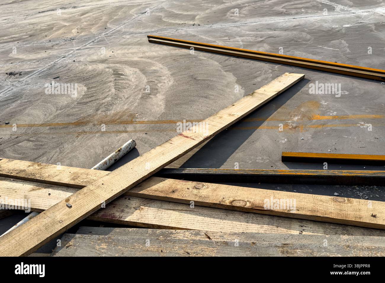 Tavole di legno e barre metalliche sparse su calcestruzzo polveroso in cantiere, vista dall'alto, luce del giorno, linee astratte e consistenza. Foto Stock