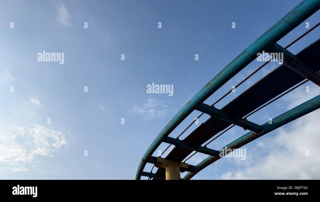 Curva minima di una pista di metallo blu arrugginita contro un cielo limpido, composizione astratta, angolo basso. Niente persone. Foto Stock