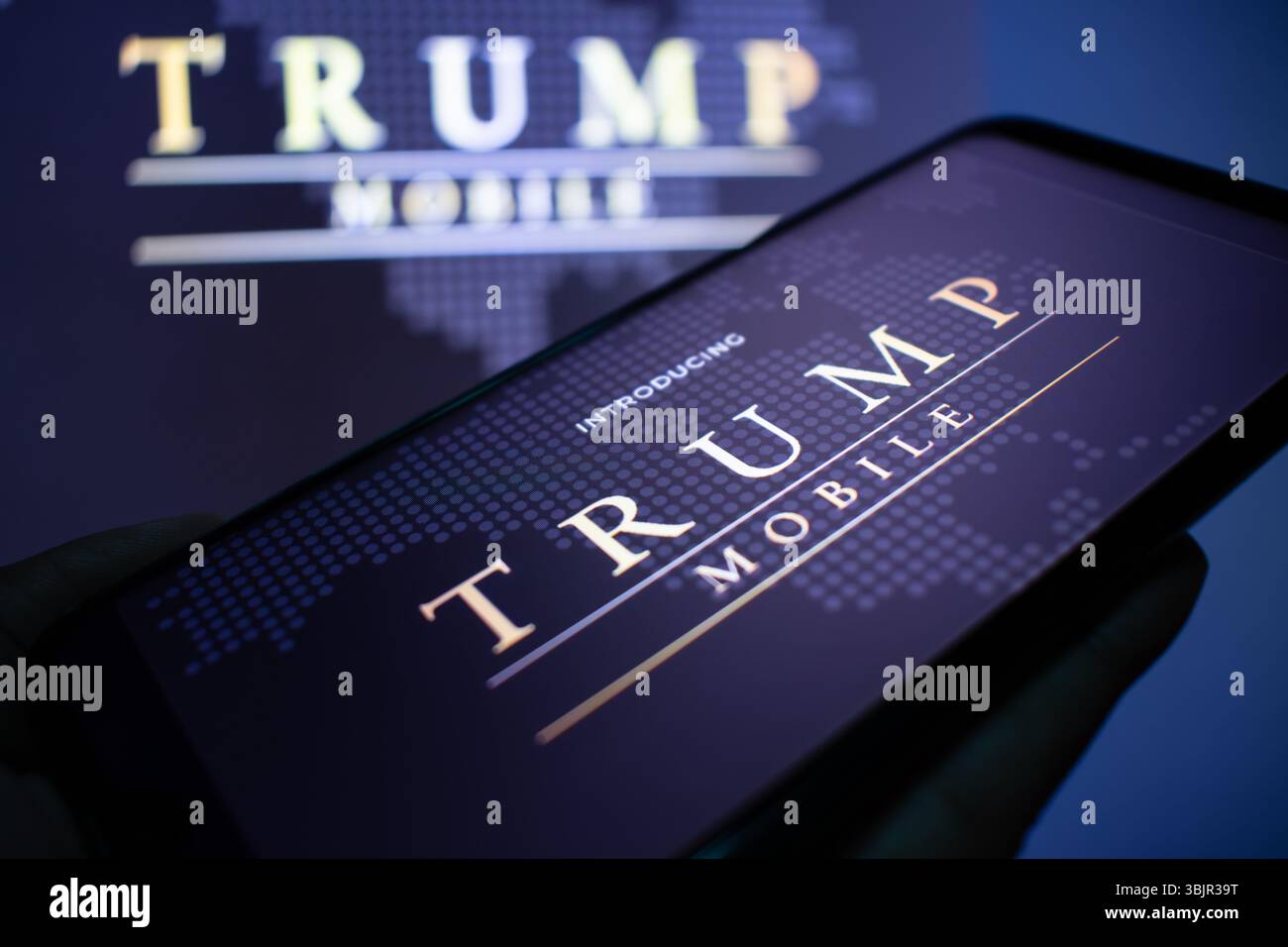 SLC, UT – 16 giugno 2025: Un uomo possiede uno smartphone che mostra il logo Trump Mobile, con un banner Trump Mobile sfocato visto sullo sfondo. Foto Stock