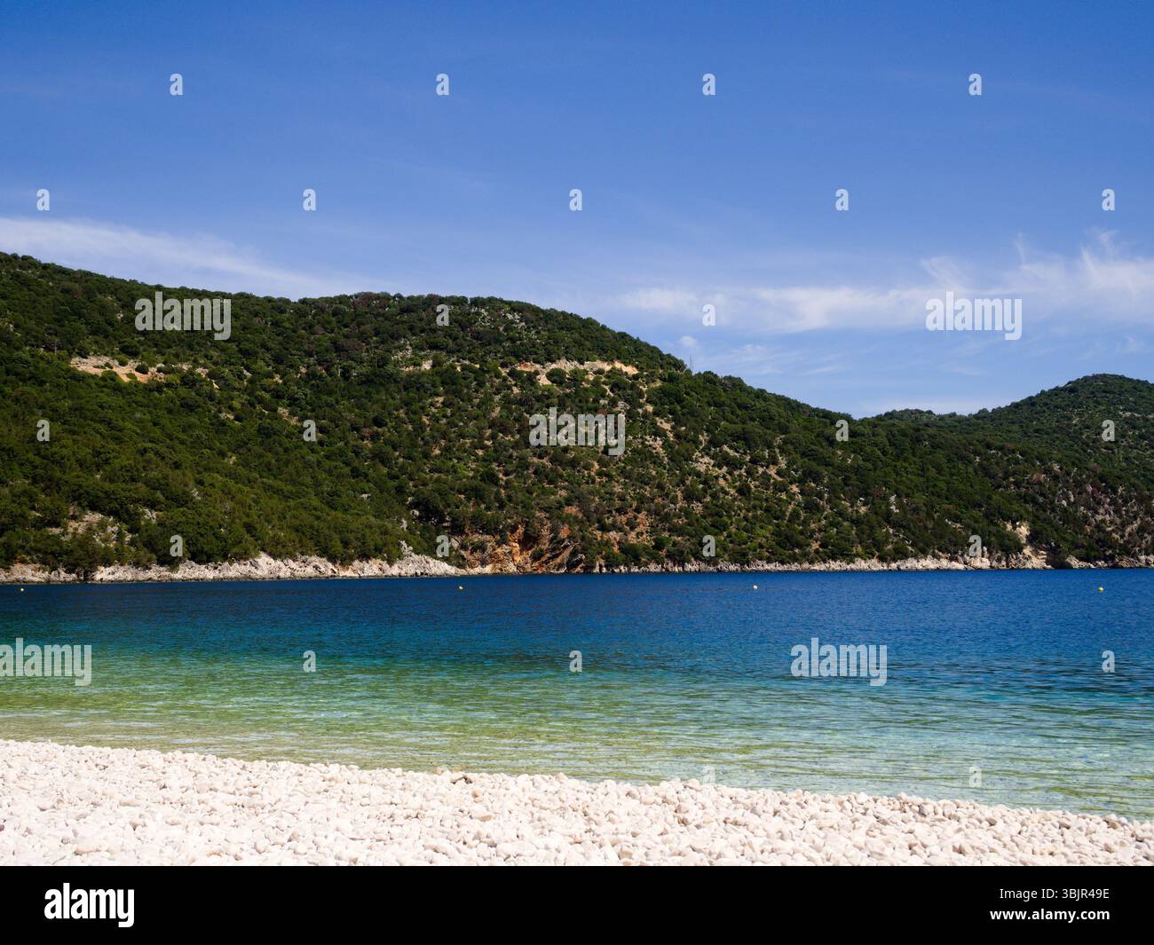 Le scogliere costiere e le vivaci acque della spiaggia di Antisamos a Cefalonia brillano sotto il sole e il cielo mediterraneo senza nuvole. Foto Stock