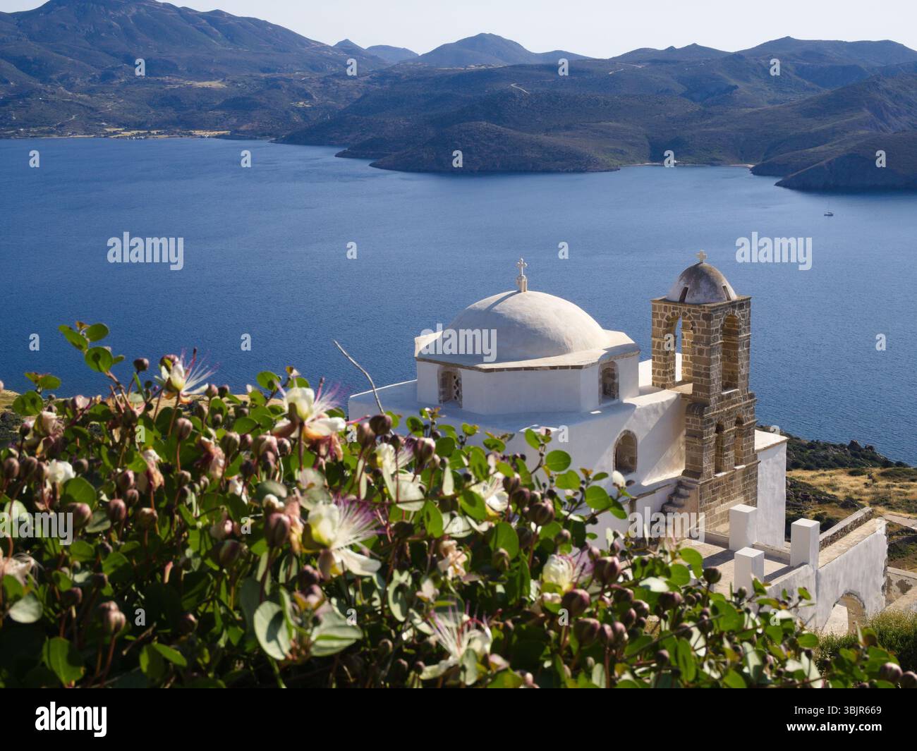 Cappella bianca minimalista e cupola sopra Plaka, Milos, che risplende nei toni del tramonto con il mare Egeo e l'aspra isola che si estende oltre. Foto Stock