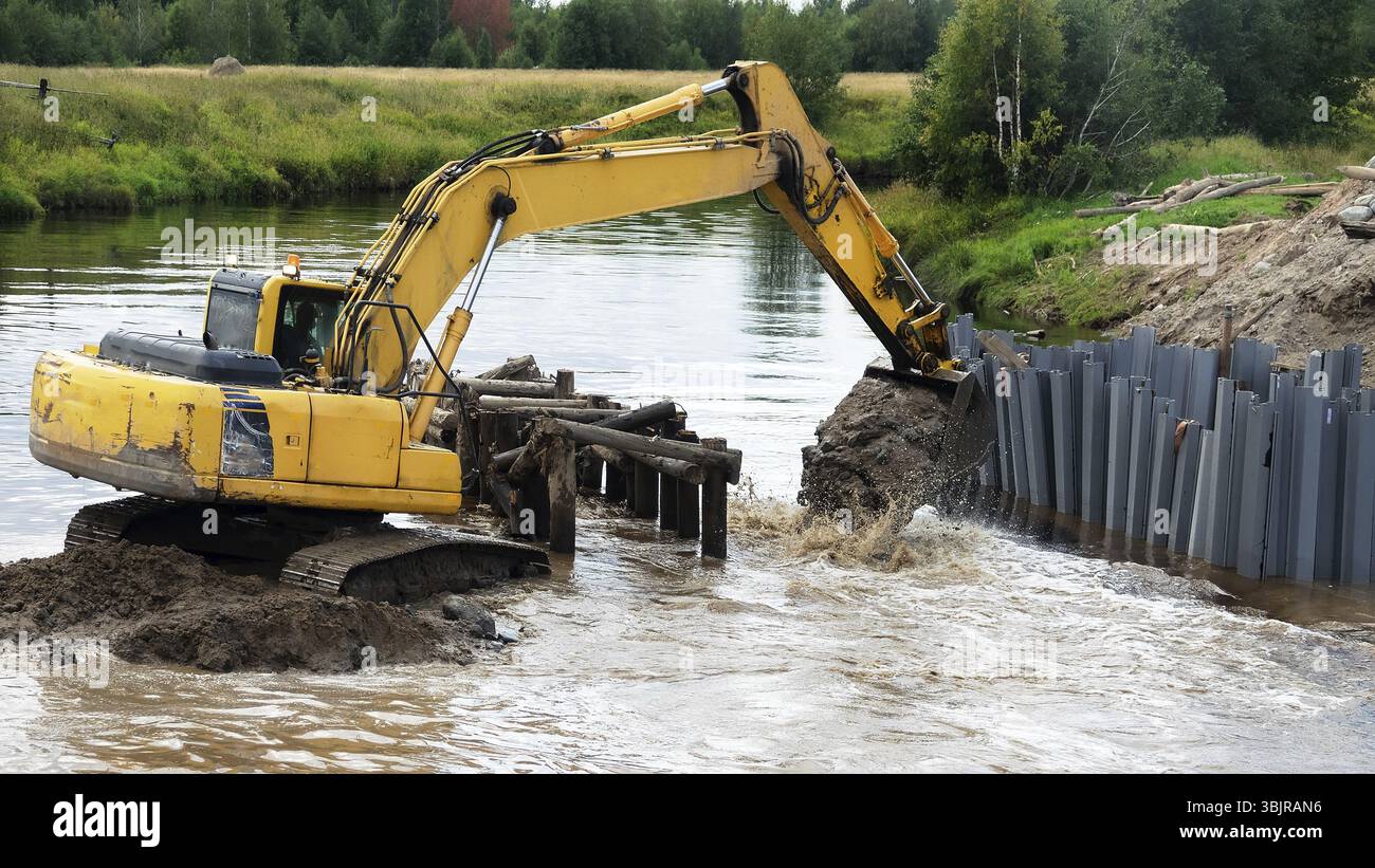 Escavatore lavora in una piccola foresta fiume, benna di un escavatore. La costruzione del nuovo ponte, ingegneria edile Foto Stock