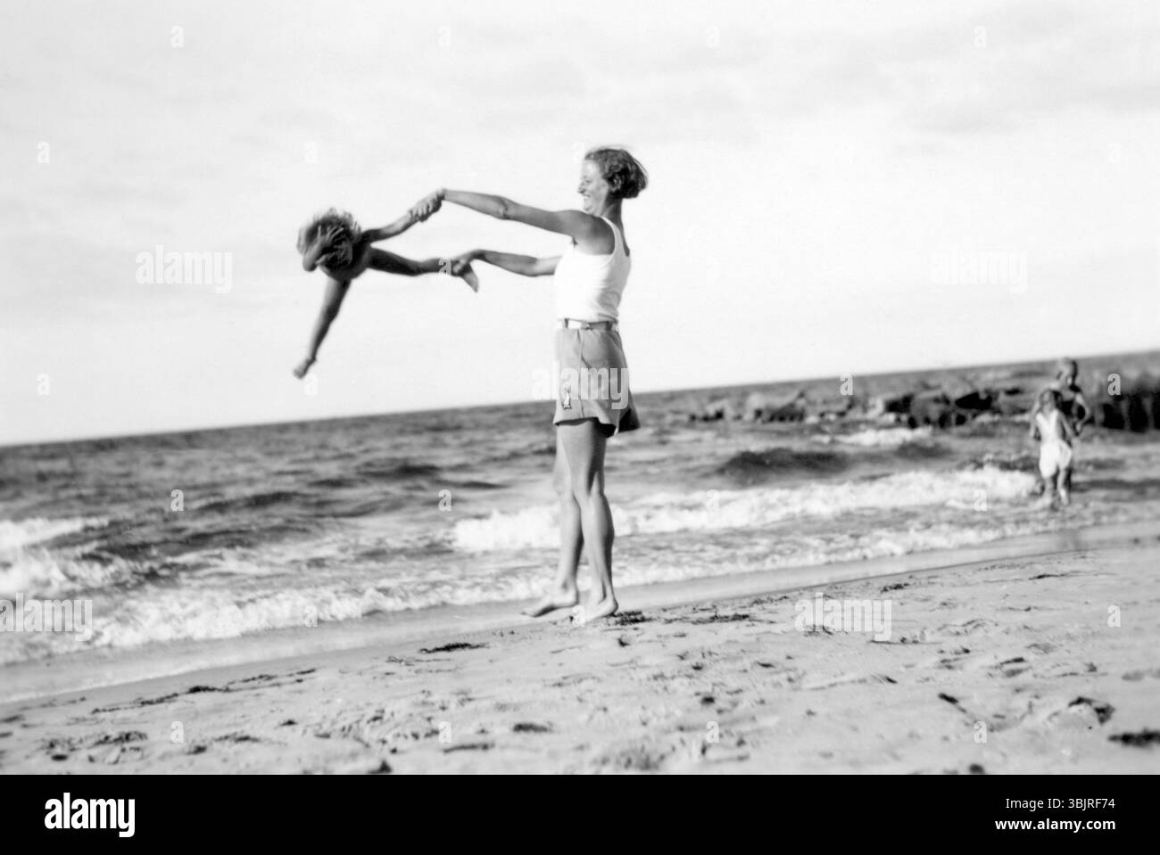 Donna con bambino sulla spiaggia, anni '1920, donna che diverte un bambino sulla spiaggia mentre il mare può essere visto sullo sfondo, foto storiche Foto Stock