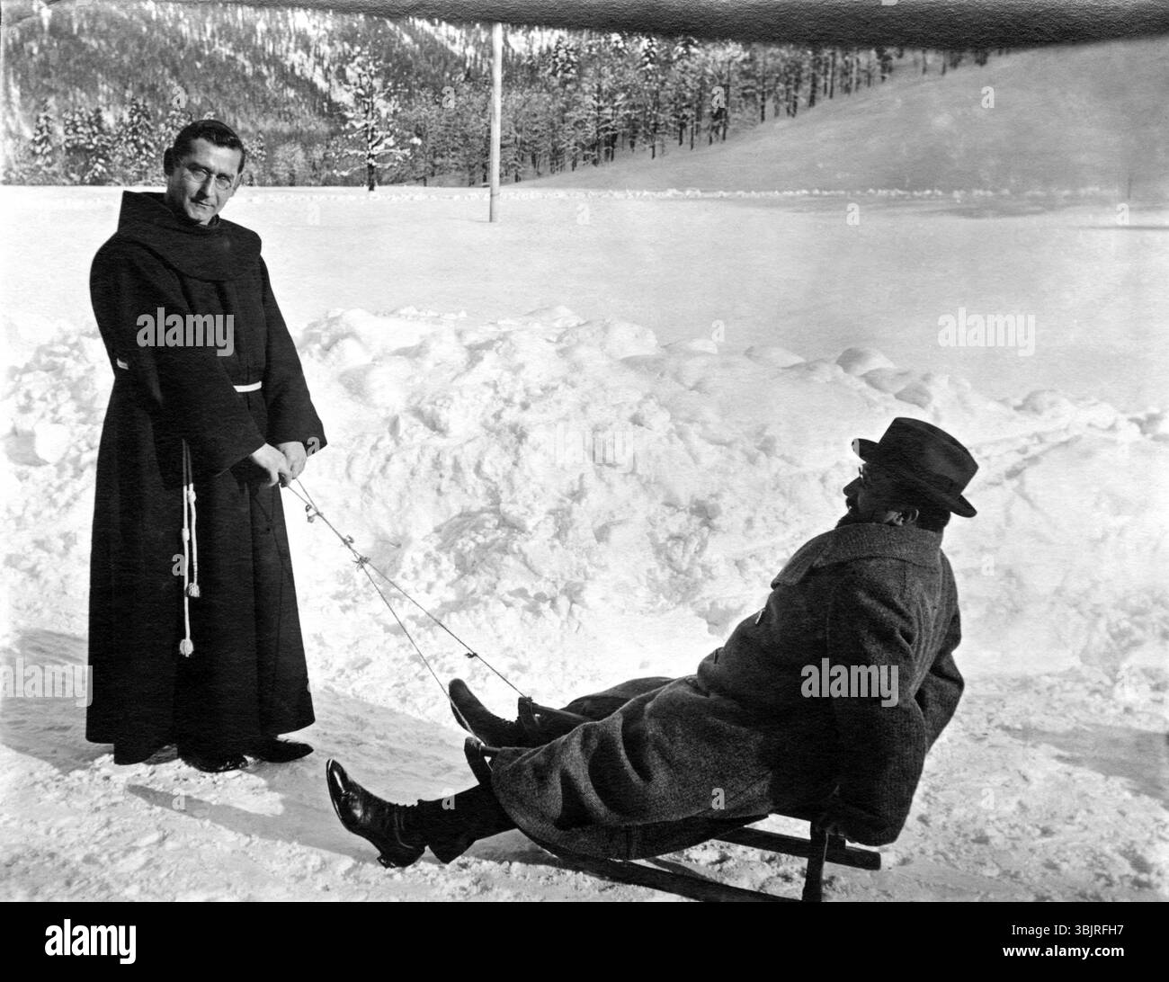 Monk and man in the Snow, anni '1920, Monk tira un uomo in abiti invernali su una slitta attraverso la neve, foto storica Foto Stock