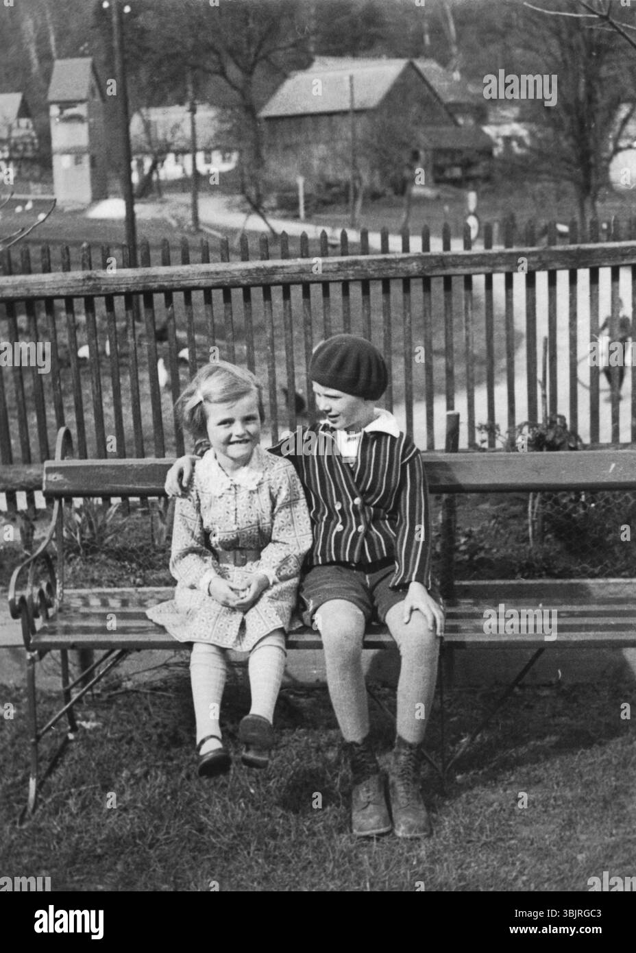 Due ragazze sedute su una panchina del parco, anni '1930, due bambini risi seduti uno accanto all'altro su una panchina in giardino, foto storica Foto Stock