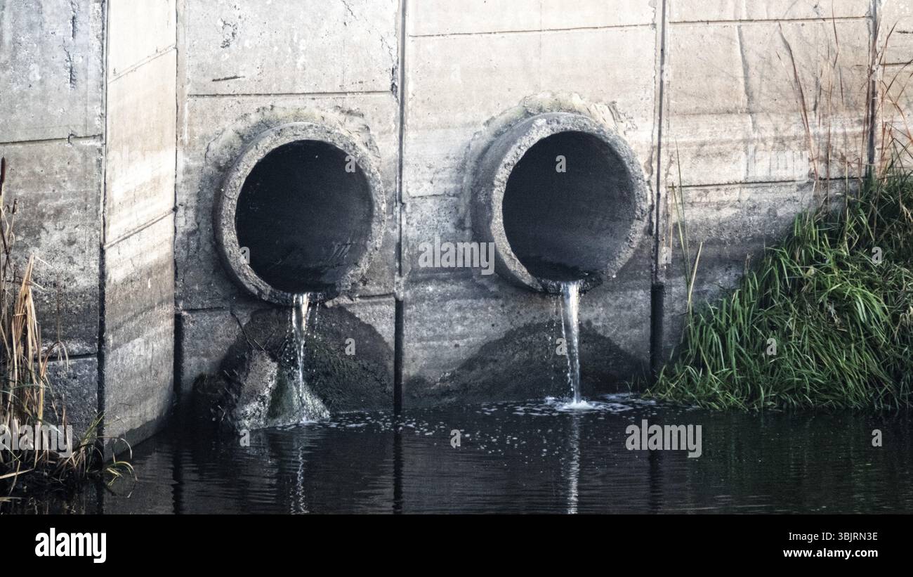 Grondaia. Deflusso d'acqua da una via di scarico (smaltimento dell'acqua, drenaggio delle tempeste), due tubi e acqua a flusso lento (deflusso diretto) dopo la pioggia Foto Stock