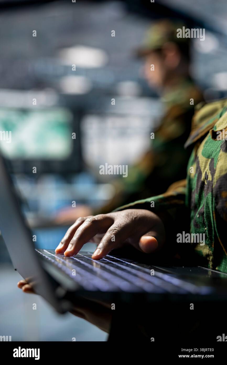Primo piano di un dipendente della sala server militare che digita sul laptop, supervisionando le configurazioni del firewall. Specialista IT dell'esercito in data center che distribuisce aggiornamenti software in strutture sicure Foto Stock