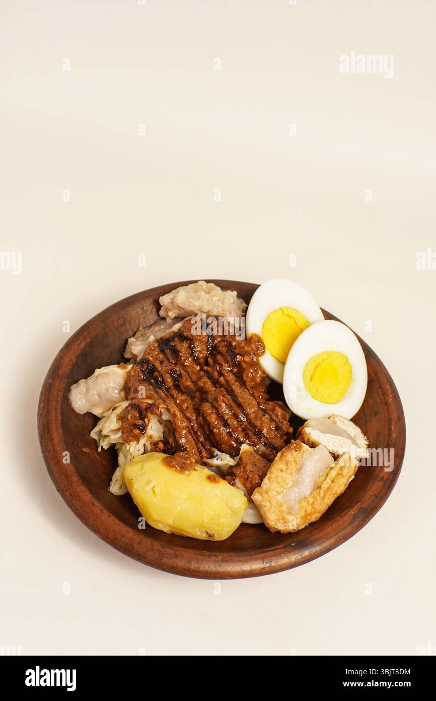 Siomay, cibo di strada indonesiano servito con patate, uova, cavolo, tofu e salsa di arachidi su un piatto di legno. Popolare piatto salato nella Giava occidentale. Foto Stock