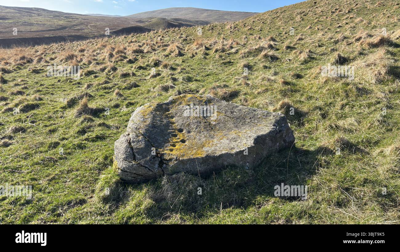 Una pietra segnata da una tazza pittica, un masso preistorico inciso con antiche depressioni di coppa e incisioni simbolo. Echi dei primi rituali nelle Highland Foto Stock