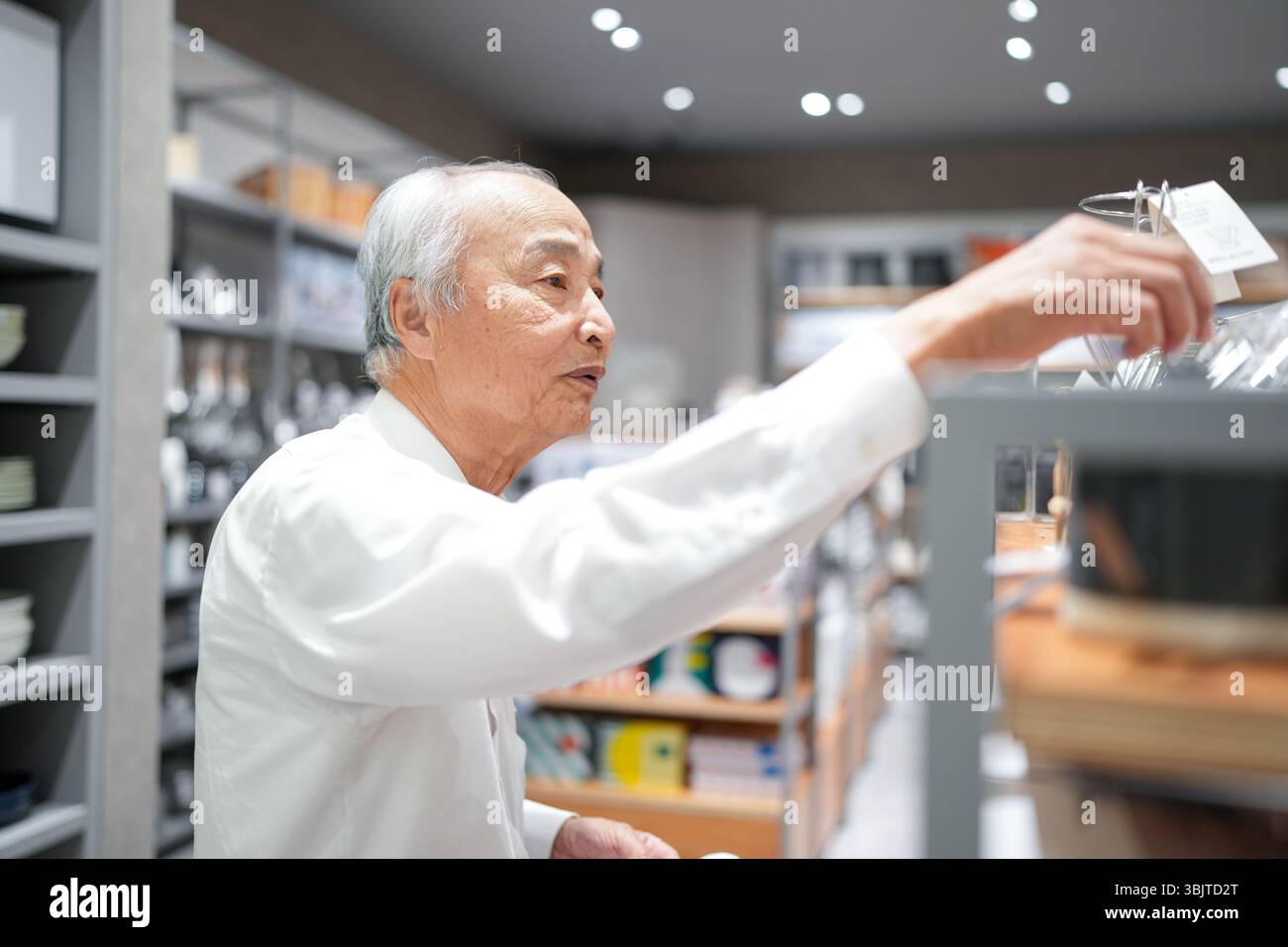 In un'elegante boutique giapponese piena di articoli per la casa, un uomo giapponese alla fine degli anni '70, che indossa una camicia bianca, sfoglia gli oggetti con un'espressione rilassata, Foto Stock