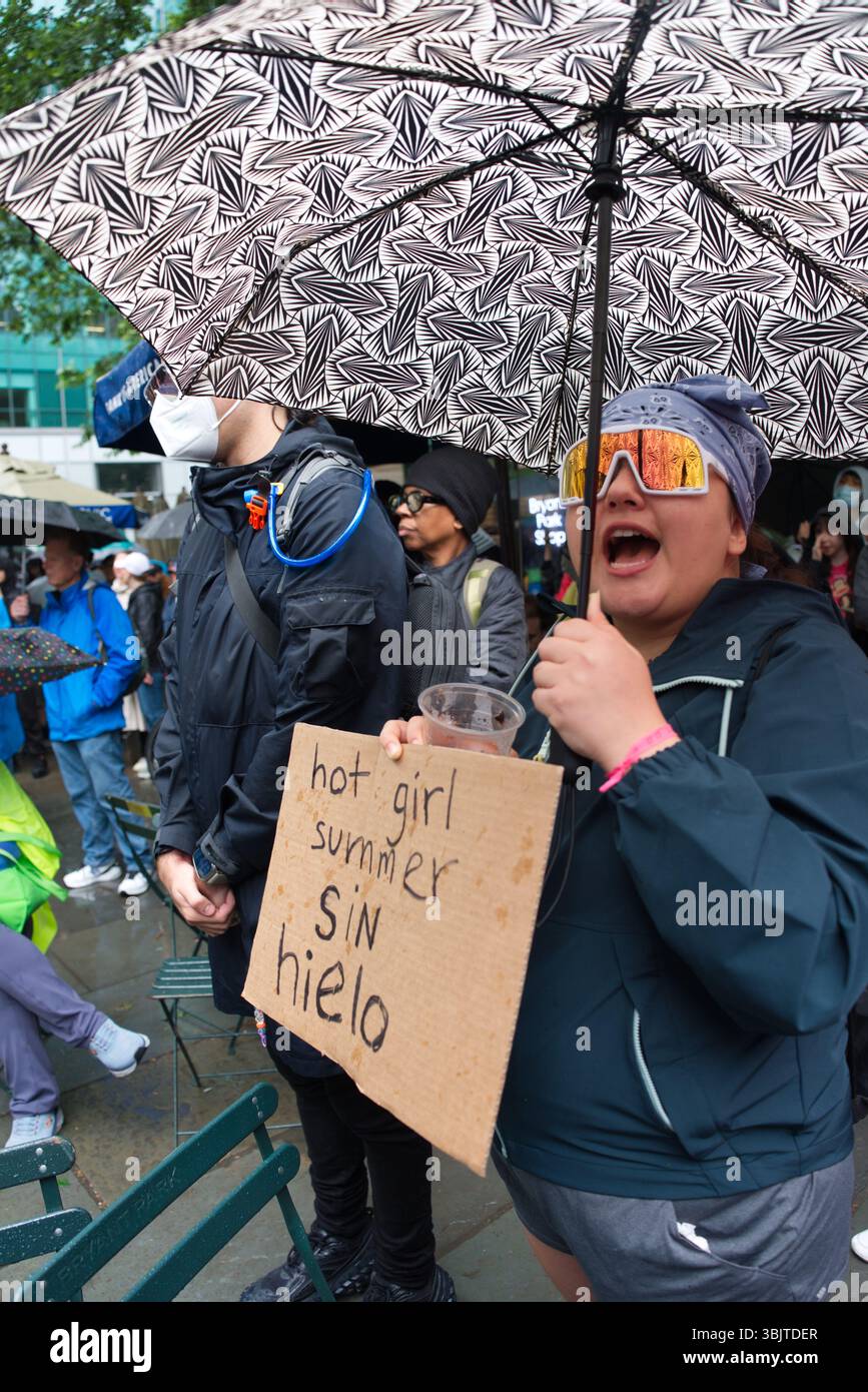 Una persona con occhiali da sole riflettenti e una bandana regge un cartello di cartone con la scritta "hot girl Summer sin hielo" sotto un ombrello a motivi durante un'uscita Foto Stock