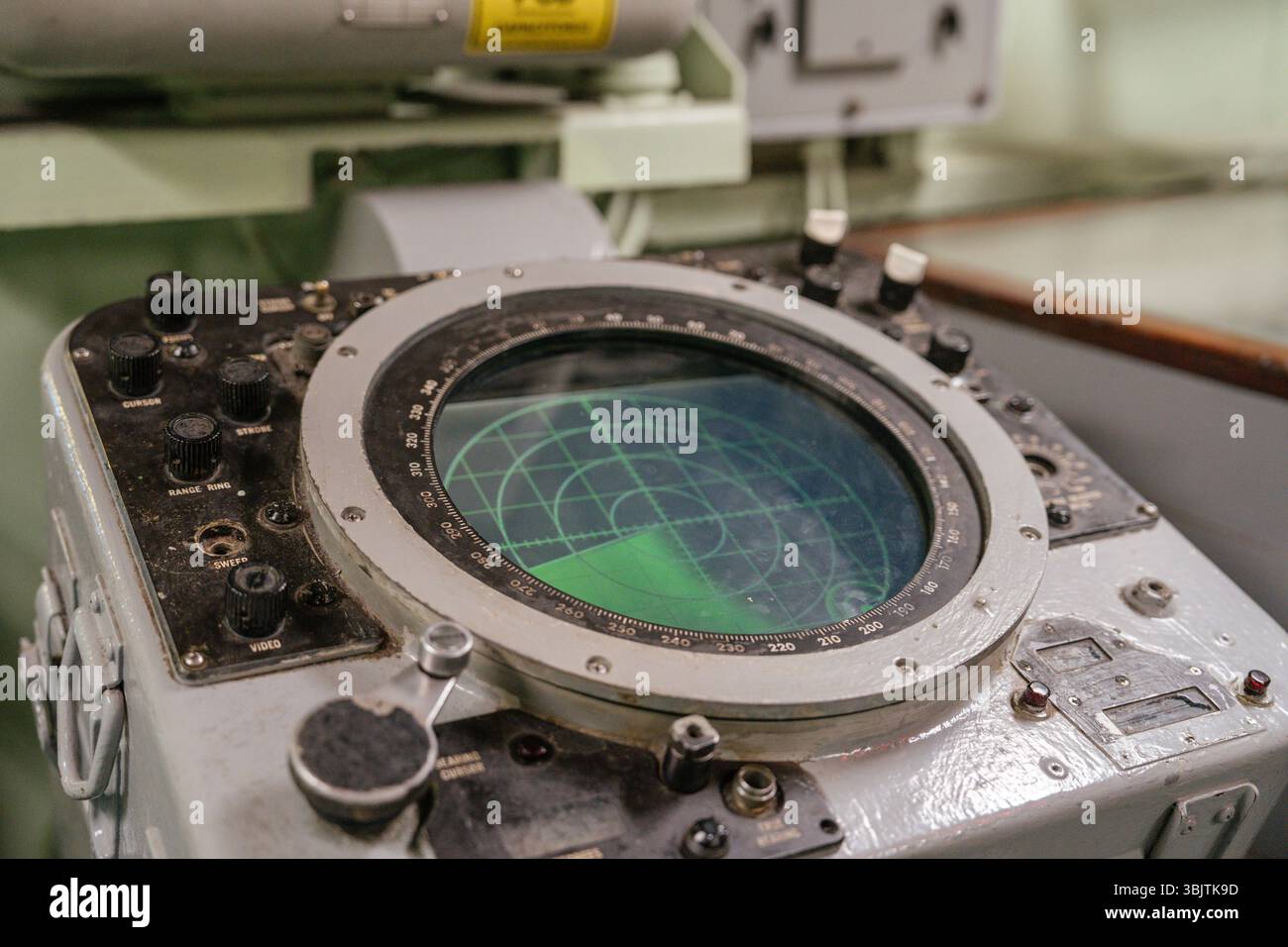 Vecchia console radar navale con schermo verde circolare e comandi meccanici. Il radar mostra una griglia di scansione utilizzata per rilevare oggetti in mare. Foto Stock