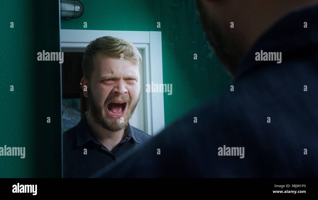 Frustrato uomo barbuto urla contro qualcuno, probabilmente in un acceso litigio, catturato al chiuso in un intenso confronto emotivo. Foto Stock