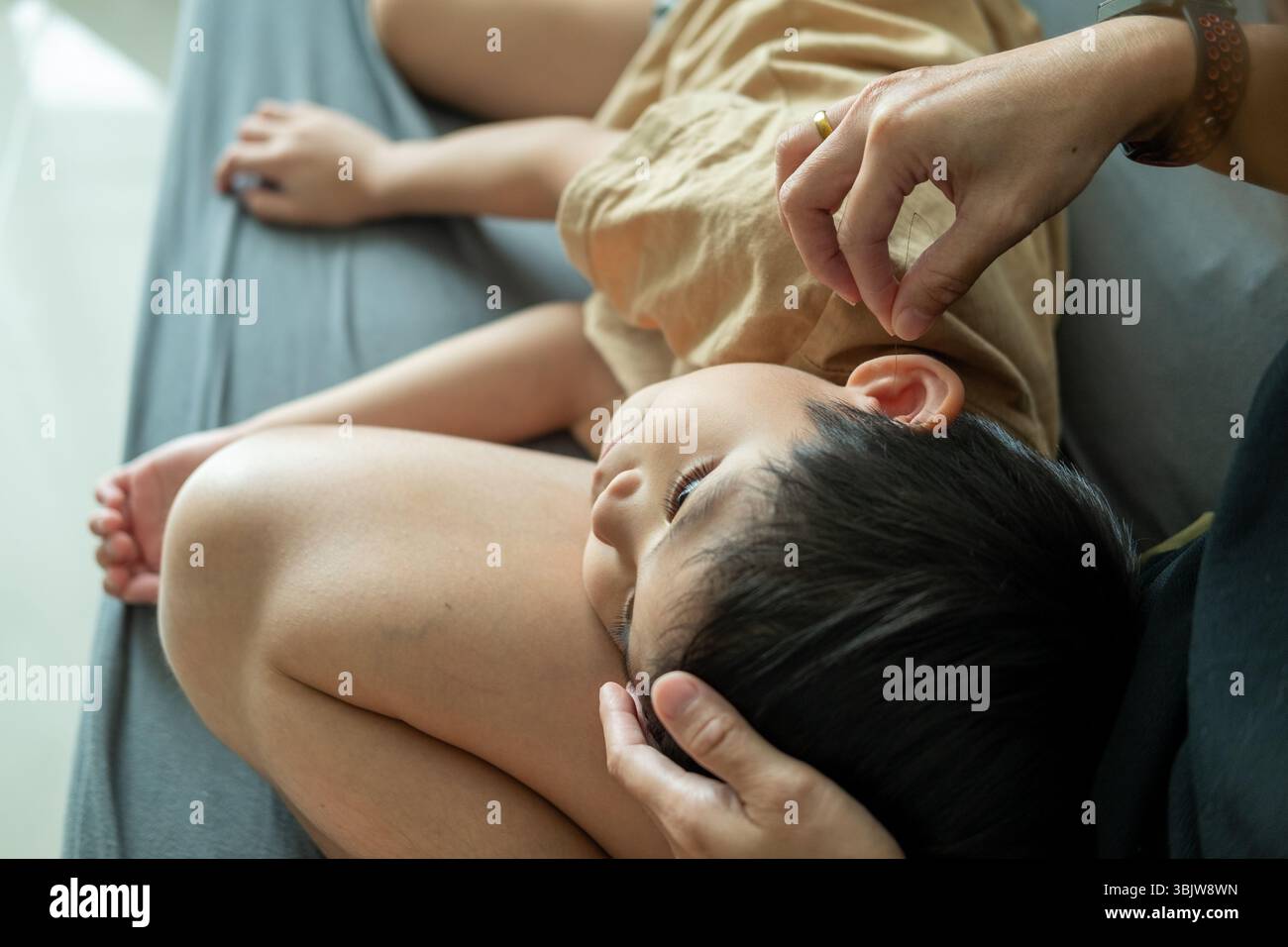Il ragazzo asiatico dorme in grembo della madre, usando i capelli per pettinarle le orecchie. Foto Stock