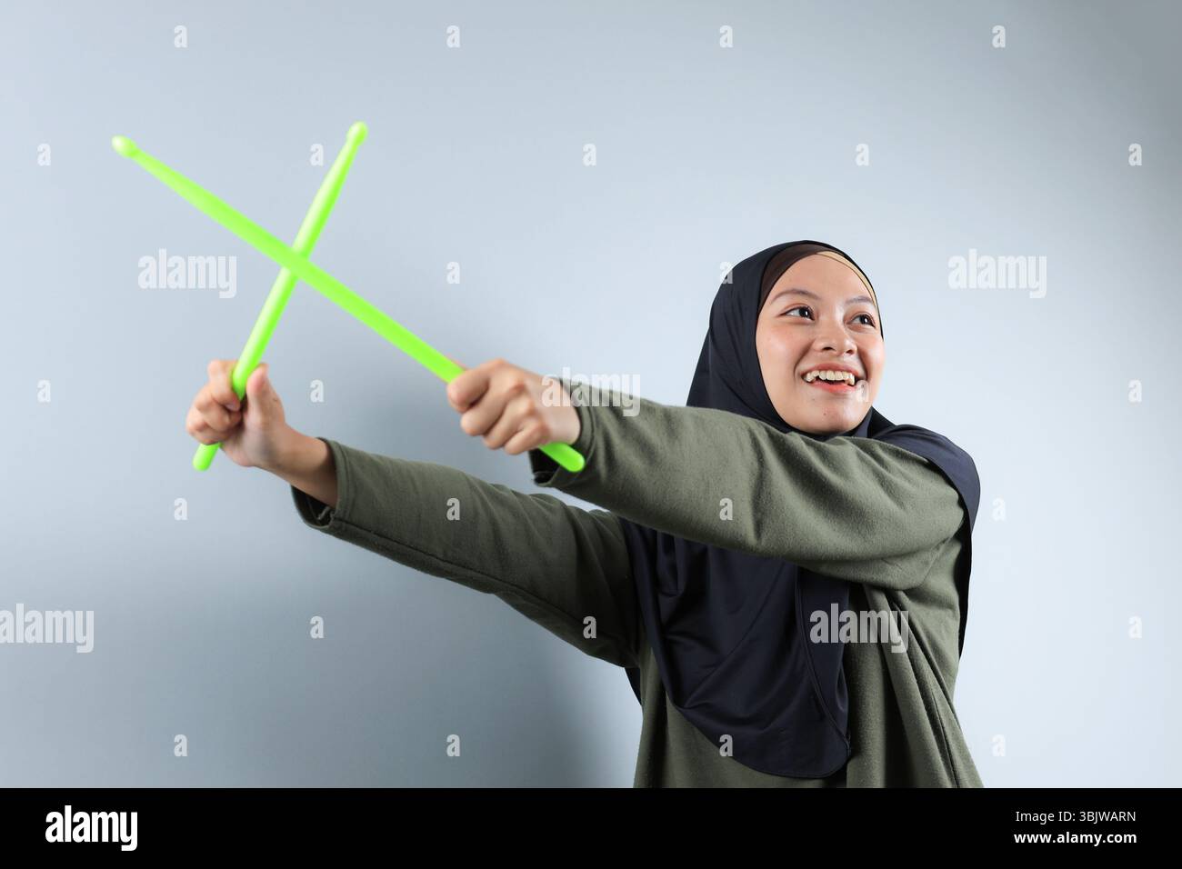 Una donna Hijabi che fa l'allenamento Pound Fit con bastoncino verde, isolata su sfondo grigio. Primo piano, angolo basso Foto Stock