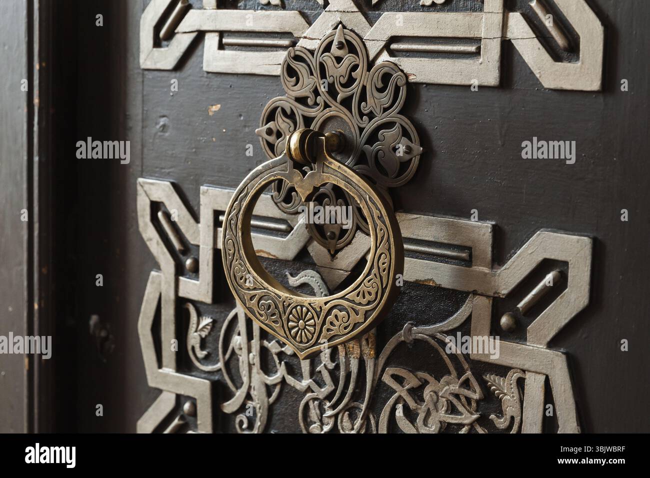 Un battitacco per porta in ottone dal design complesso fissato a una porta in legno tradizionale, impreziosito da dettagli geometrici e decorati floreali Foto Stock