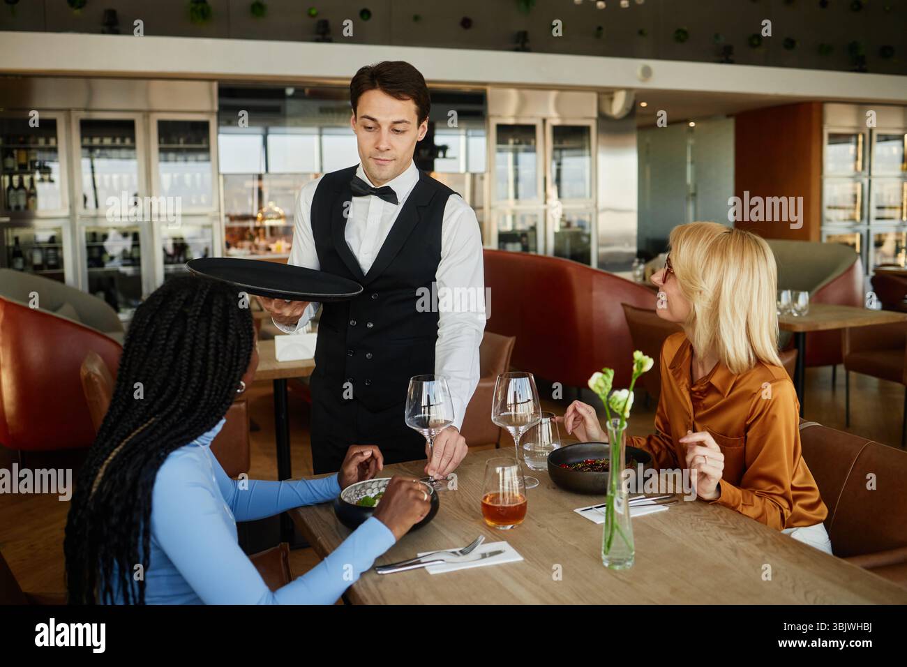 Giovane uomo caucasico che serve cibo per diverse giovani donne nel moderno ristorante Foto Stock