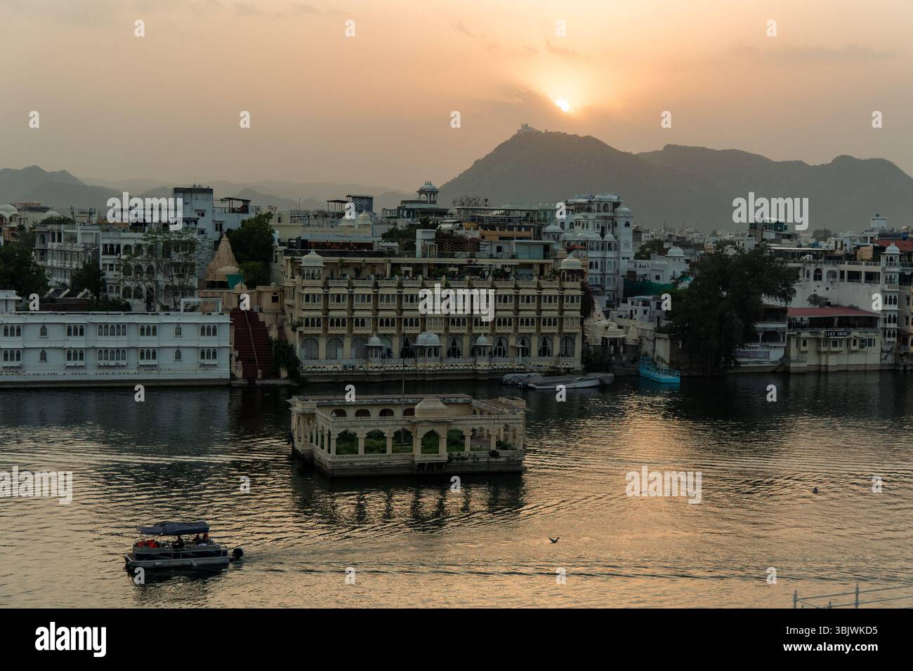 Tramonto dorato sul lago Pichola che illumina il Palazzo della città di Udaipur, il Lake Palace Hotel e Jag Mandir con barche che navigano nelle acque calme e la bocca Foto Stock
