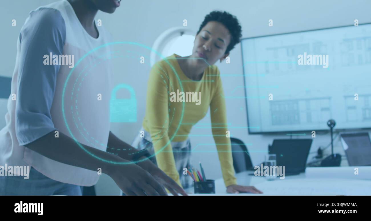 Due donne d'affari che esaminano i documenti al tavolo dell'ufficio, con laptop e lucchetto olografico Foto Stock