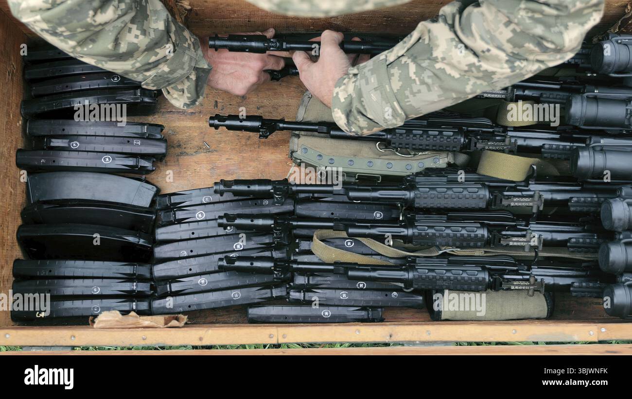 Personale militare che maneggia armi da fuoco e munizioni. Vista dall'alto del personale militare che maneggia più armi da fuoco e riviste in una cassa di legno. Foto Stock