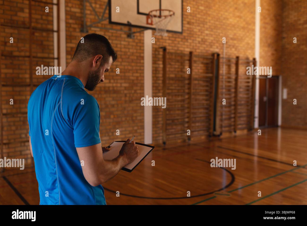La corte in legno è illuminata sotto le luci superiori, mostrando linee del pavimento dipinte, canestro e barre sulle pareti Foto Stock