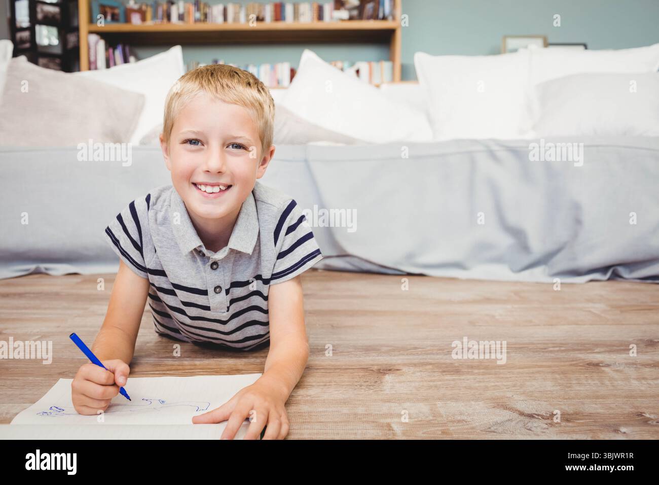 Ragazzo in età scolastica che indossa un disegno a polo a righe con un pennarello blu su carta nel soggiorno Foto Stock