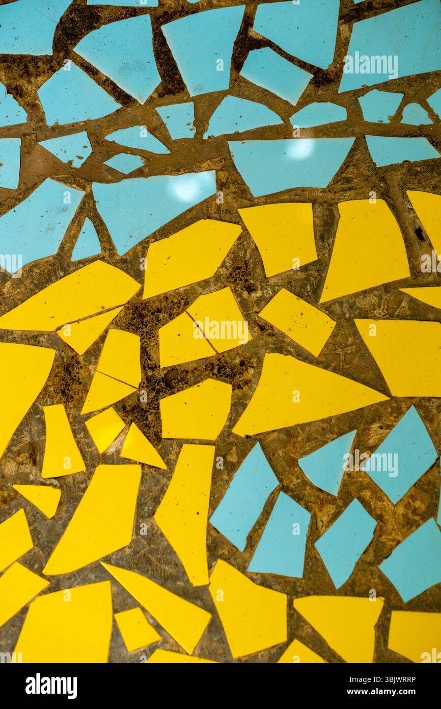 Mosaico di piastrelle gialle e blu con un quadrato blu al centro. Le piastrelle sono rotte e sparse sulla superficie Foto Stock