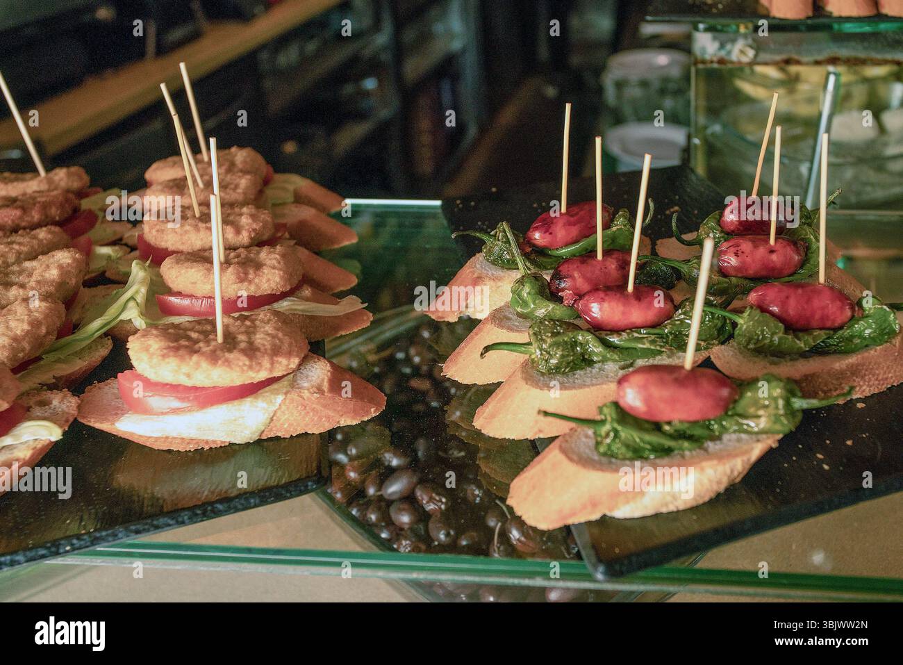 tapas (pintxos, panino) con salsiccia piccola e peperoni salati, pane e spiedini di legno e tapas con una cotoletta (pollo?) e affettato il pomodoro in Foto Stock
