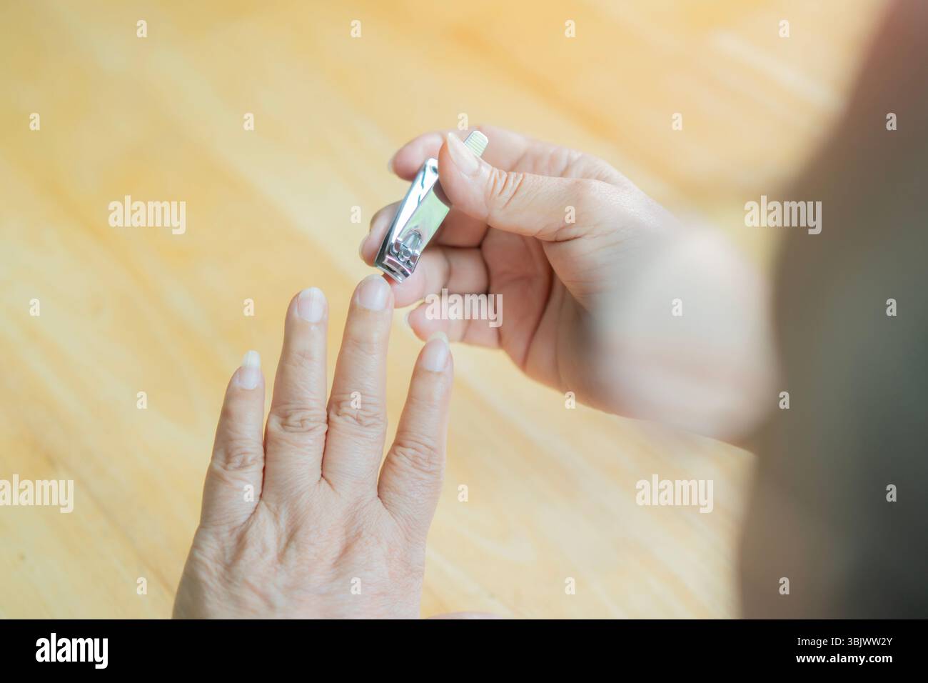 Vista posteriore delle mani di una donna anziana con il taglio delle unghie su un tavolo in legno. Concetto di chiodo da taglio. copia spazio. Foto Stock