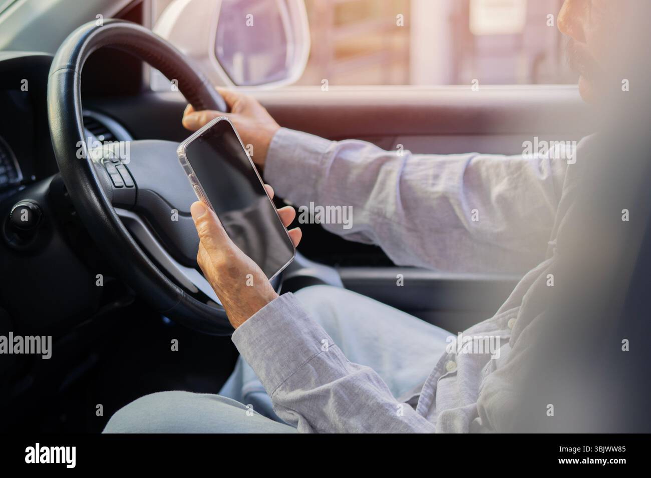 Vista laterale del vecchio guida la sua auto mentre utilizza o guarda il telefono cellulare. Guida pericolosa su strada Foto Stock