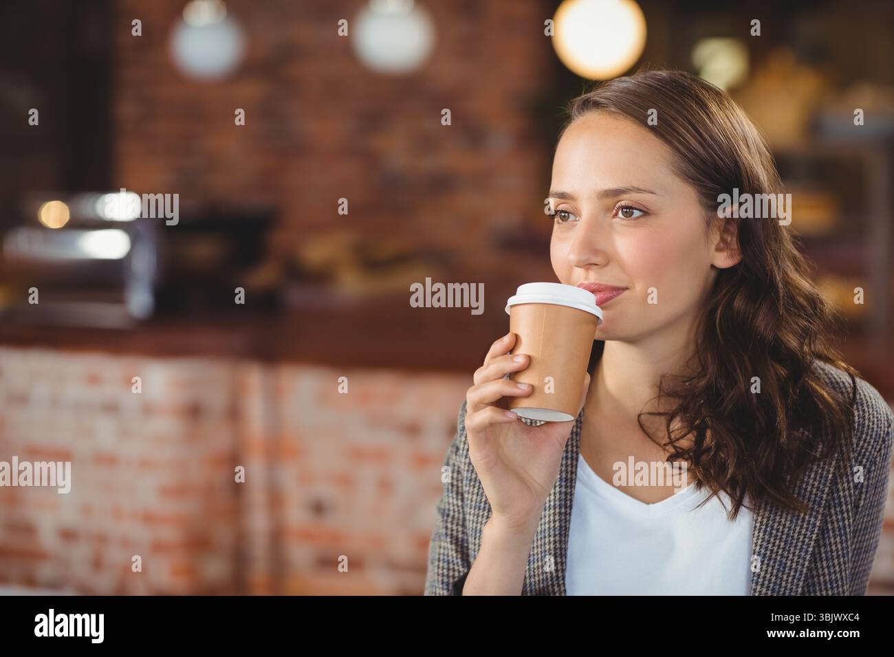 Tazza di caffè usa e getta con vapore su un bancone in legno contro le pareti in mattoni con calde luci a globo Foto Stock
