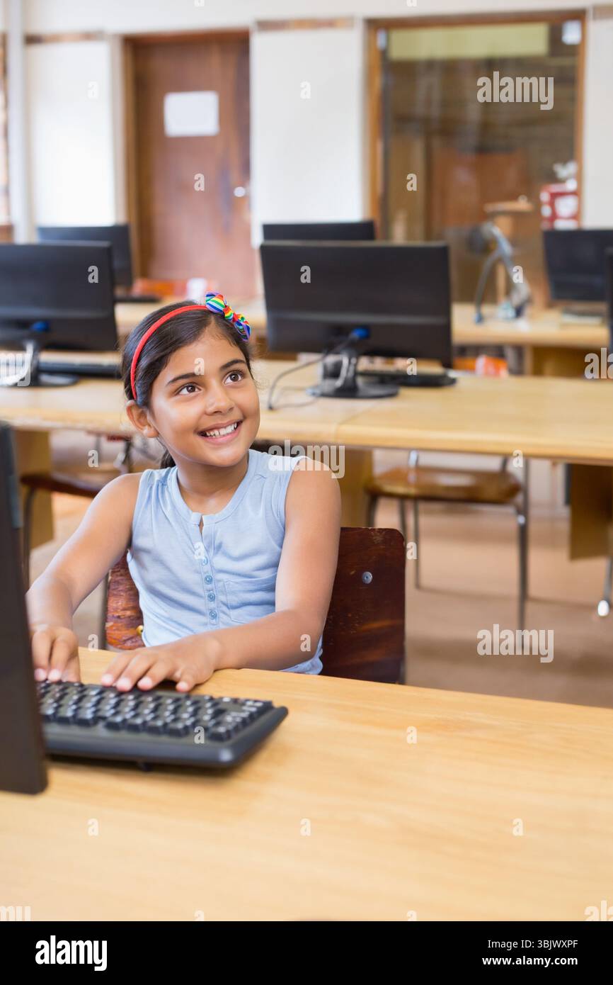 Bambina indiana che digita sulla tastiera nel laboratorio di computer della scuola con monitor desktop e scrivania in legno Foto Stock