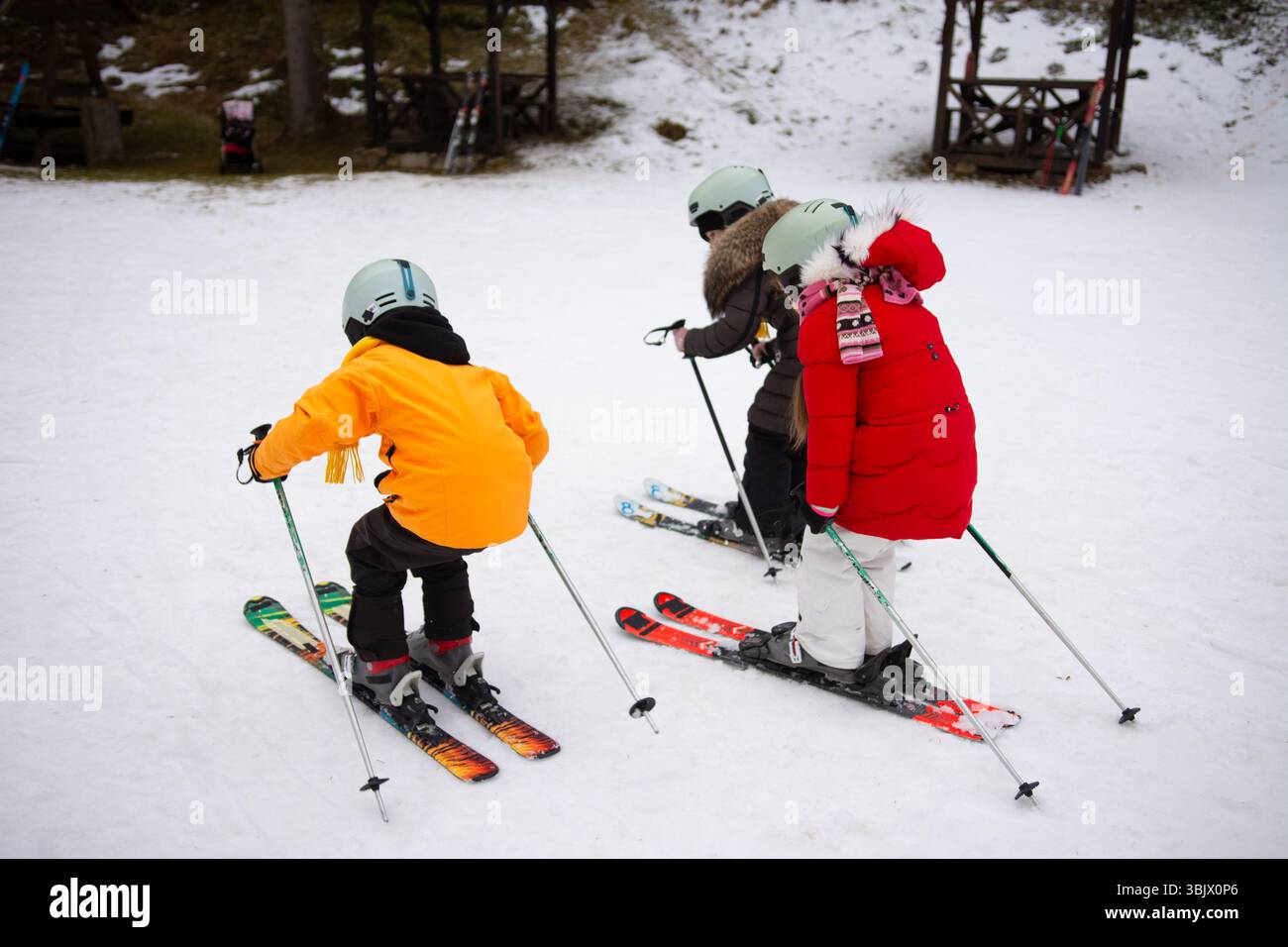 Tre bambini praticano le loro abilità sciistiche su una pista innevata, indossando abiti e caschi luminosi, trascorrendo un divertente pomeriggio invernale in una stazione sciistica. Foto Stock
