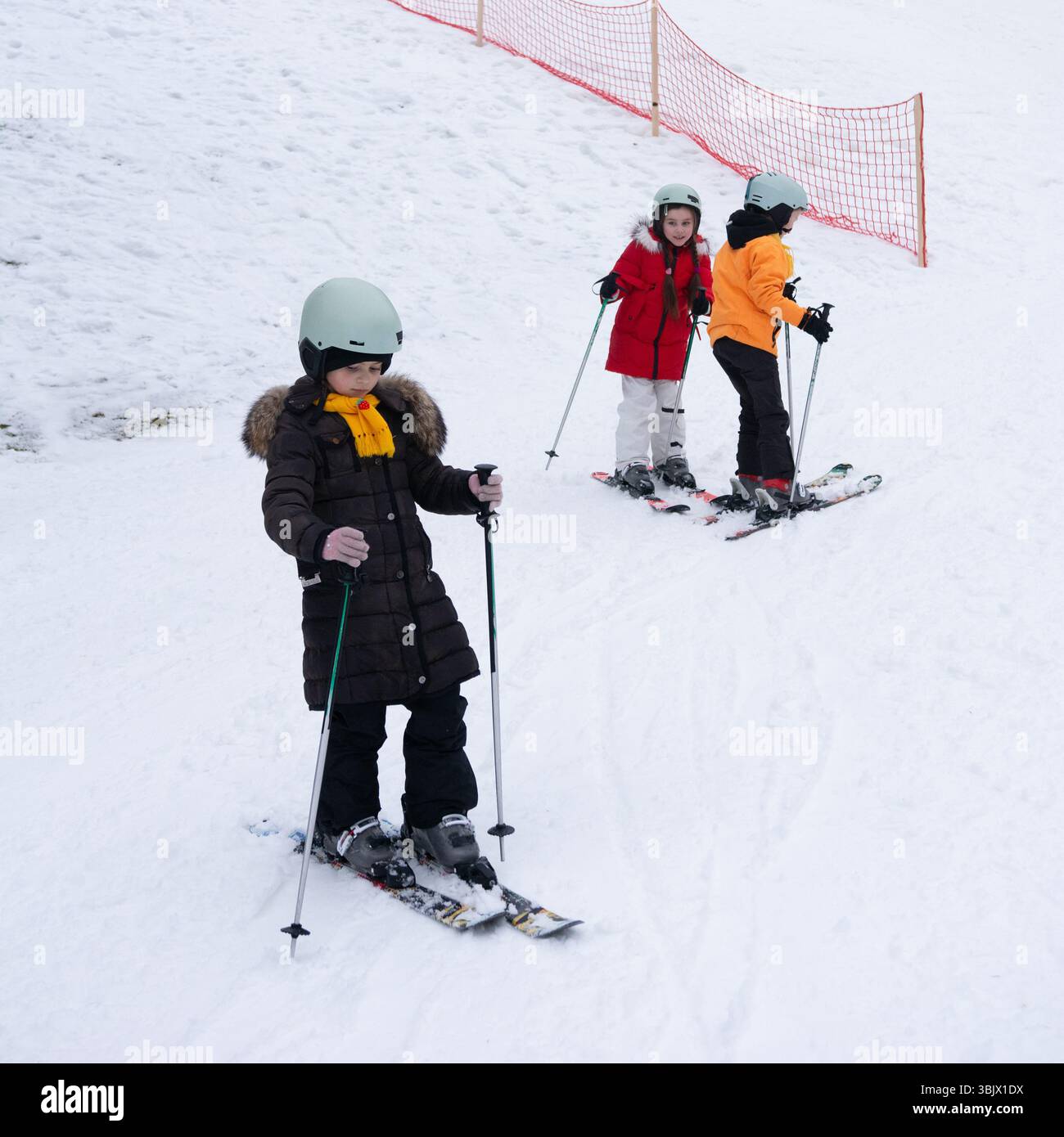 I bambini prendono le prime lezioni di sci, scivolando lungo una pista innevata con abiti e caschi colorati. Risate e divertimento riempiono l'aria frizzante dell'inverno Foto Stock