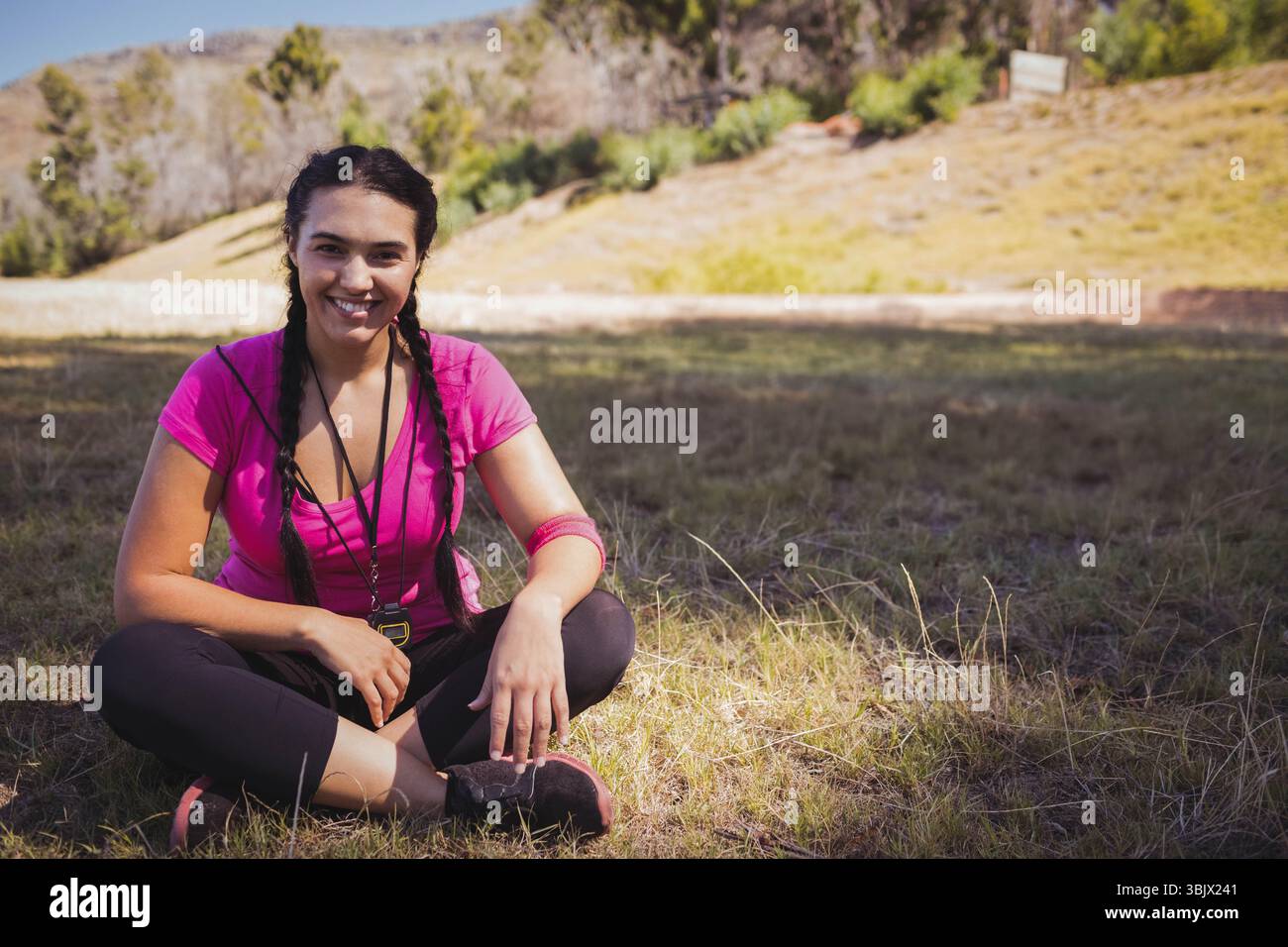 donna ventenne seduta a gambe incrociate nel prato con fascia antisudore che tiene fischietto vicino alle sneakers Foto Stock
